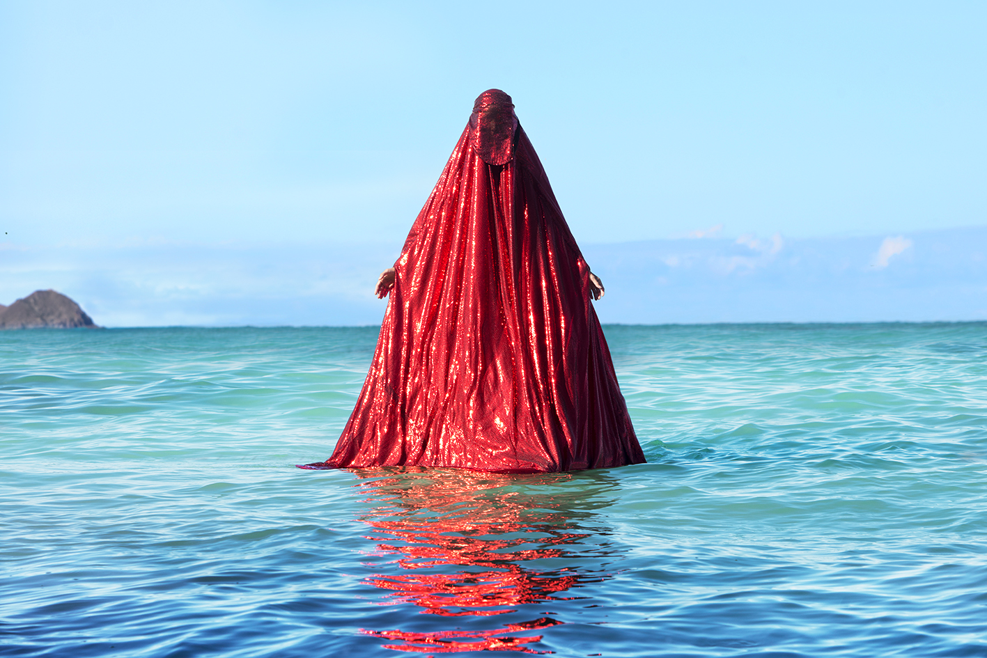 Woman cloaked in red appearing to stand on top of the ocean water