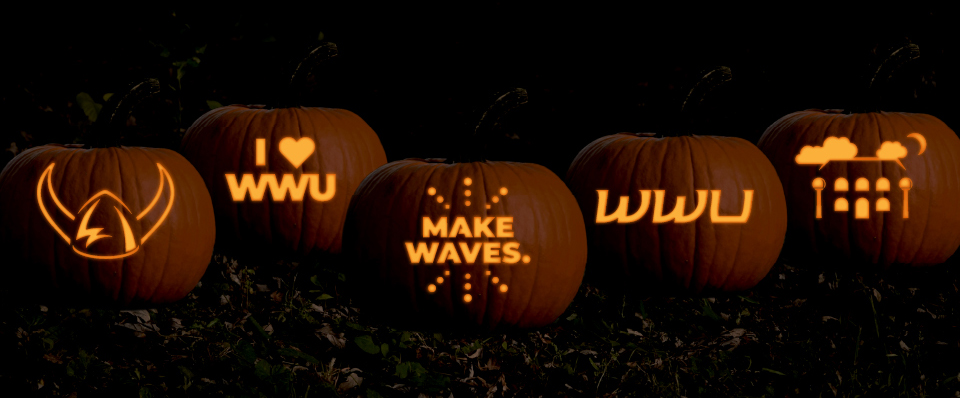 A row of jack-o-lanterns with carvings of various Western symbols: a viking hat, I heart WWU, Make Waves, WWU, and Old Main