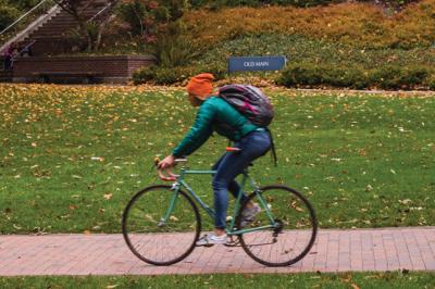 A student commutes by bike along a brick path in front of Old Main.