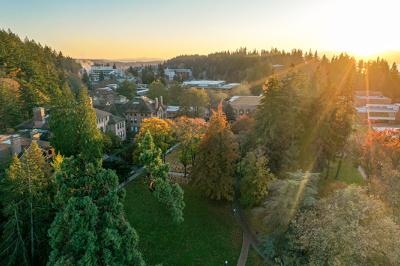 An aerial view of the sun casting rays of light over the campus as it sets with islands and ocean in the backdrop.
