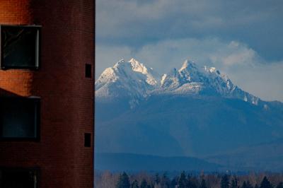 Snowy rugged peaks of the Canada's North Shore Mountain Range rise beyond the curved red brick corner of Mathes Hall.