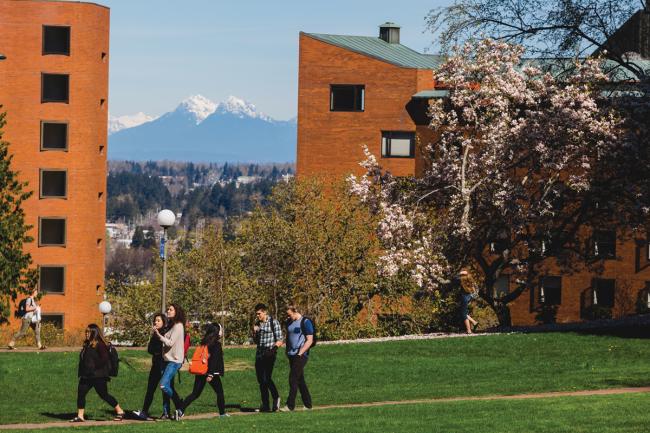 A small group of students walk together in front of Mathes Hall and Nash Hall towards the VU Dining Commons. There is a view of Mt. Baker between the two Residence Halls. 