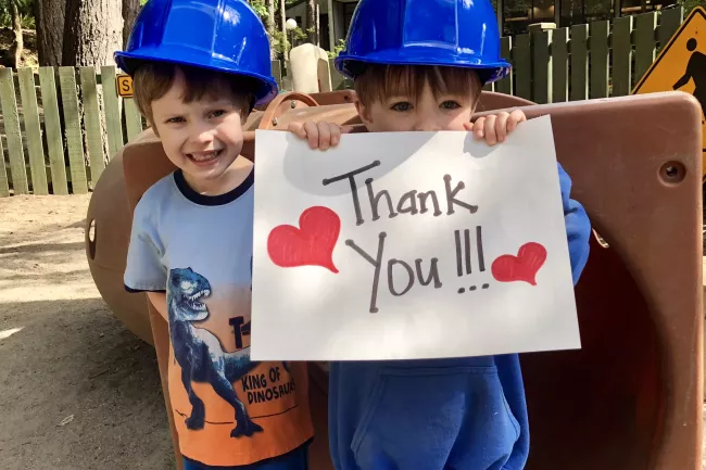 Two young children from the WWU Associated Students Child Development Center in blue hard hats holding a sign with red hearts that says thank you, from WWU give day. 