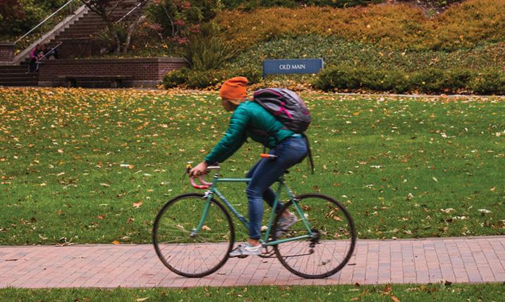 A student commutes by bike along a brick path in front of Old Main.