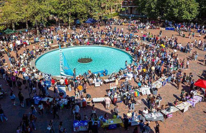 an aerial view of red square on a sunny day with the blue fountain and many people gathered and tables out for an info fair